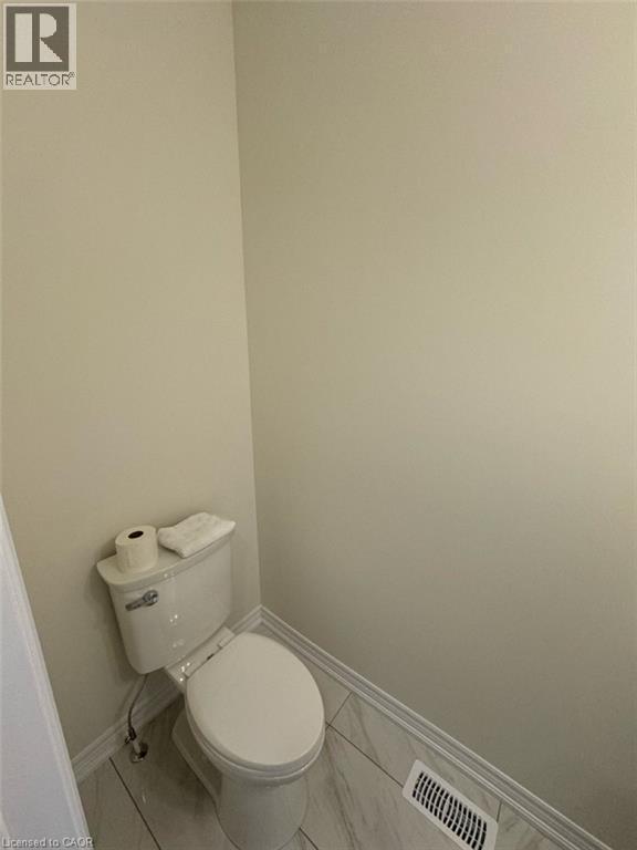 White porcelain toilet, light neutral wall paint, white baseboards, and patterned floor tiling - 10 Guernsey Drive Unit# Upper, Kitchener, ON