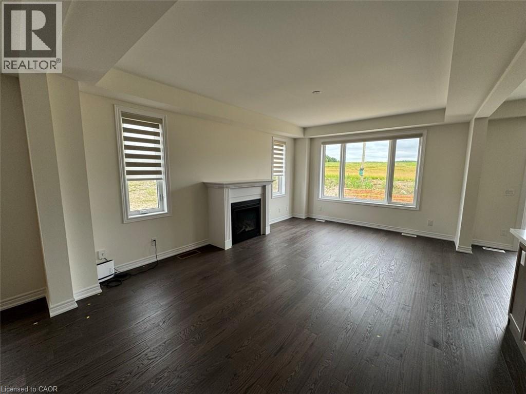 Spacious living area featuring dark wood-finish flooring, a contemporary electric fireplace with a white mantel, and large windows providing ample natural light - 10 Guernsey Drive Unit# Upper, Kitchener, ON