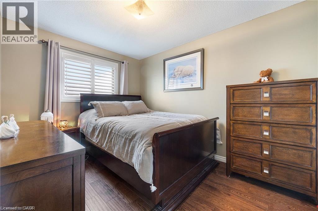Bedroom featuring wood-finish flooring, neutral wall tones, and a window with white plantation shutters - 125 Terni Boulevard, Hamilton, ON