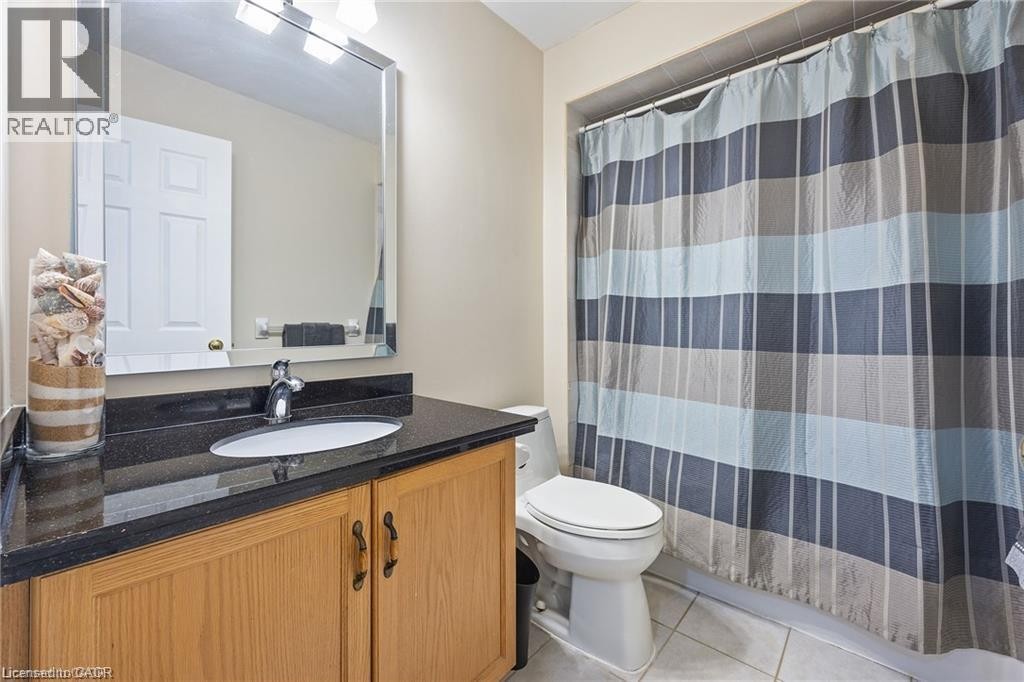 Bathroom featuring a wood-finish vanity with dark countertop, undermount sink, and polished chrome faucet - 125 Terni Boulevard, Hamilton, ON - Indoor Photo Showing Bathroom