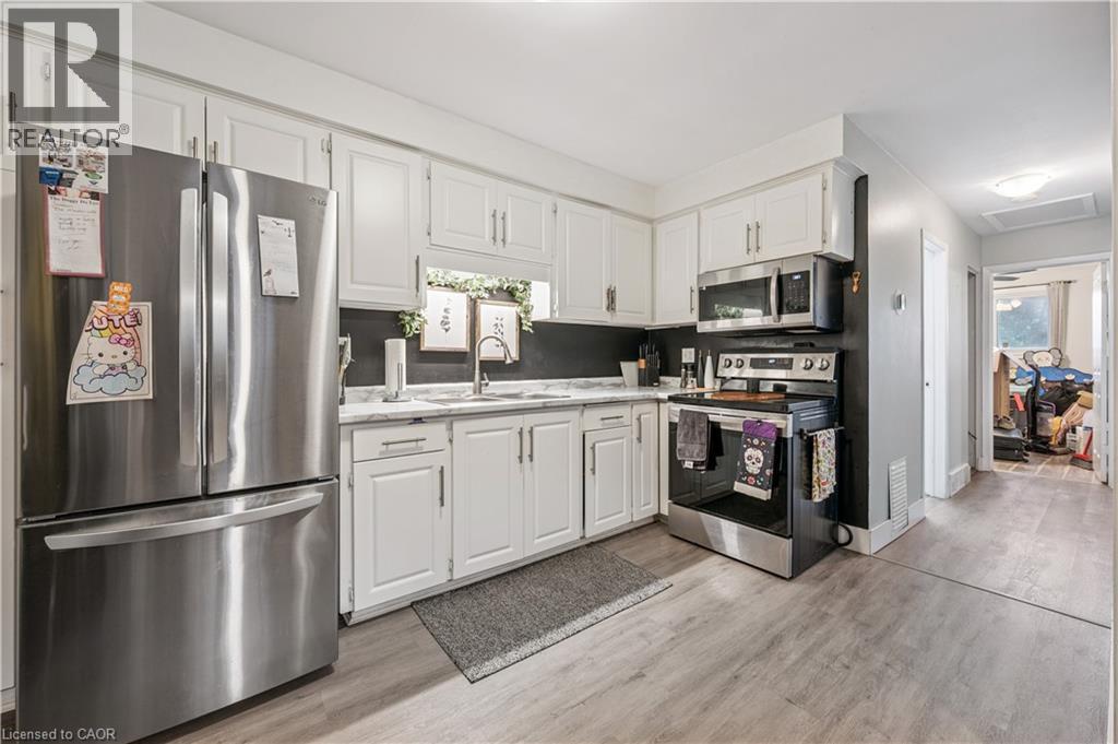 Kitchen featuring white cabinetry, stainless steel appliances, light-toned wood-finish flooring, and a window above the sink - 35 Vicmount Drive, Kitchener, ON