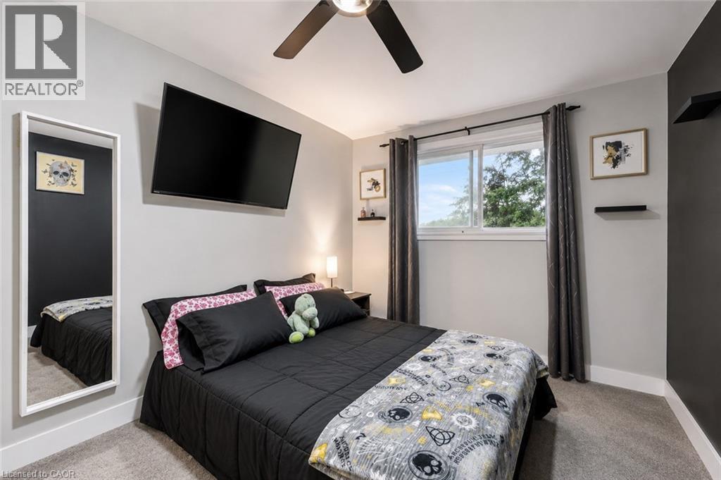 Carpeted room featuring a ceiling fan, a wall-mounted television, and a window with a dark curtain rod. Digitally enhanced. - 35 Vicmount Drive, Kitchener, ON