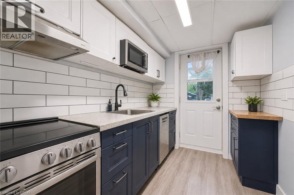 Modern kitchen featuring stainless steel appliances, two-tone cabinetry with black hardware, white subway tile backsplash, light-toned countertops, and wood-finish flooring. Digitally enhanced. - 35 Vicmount Drive, Kitchener, ON