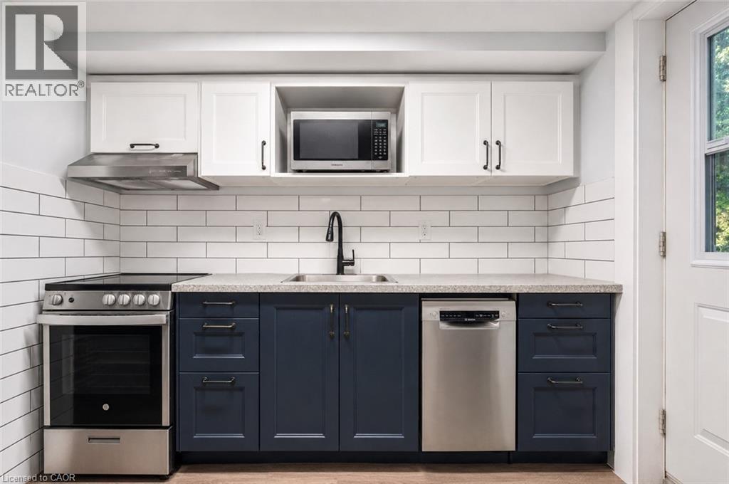 Modern kitchen featuring stainless steel. appliances, crisp white subway tile backsplash, white upper cabinetry, and contrasting navy lower cabinetry with dark hardware. Digitally enhanced. - 35 Vicmount Drive, Kitchener, ON