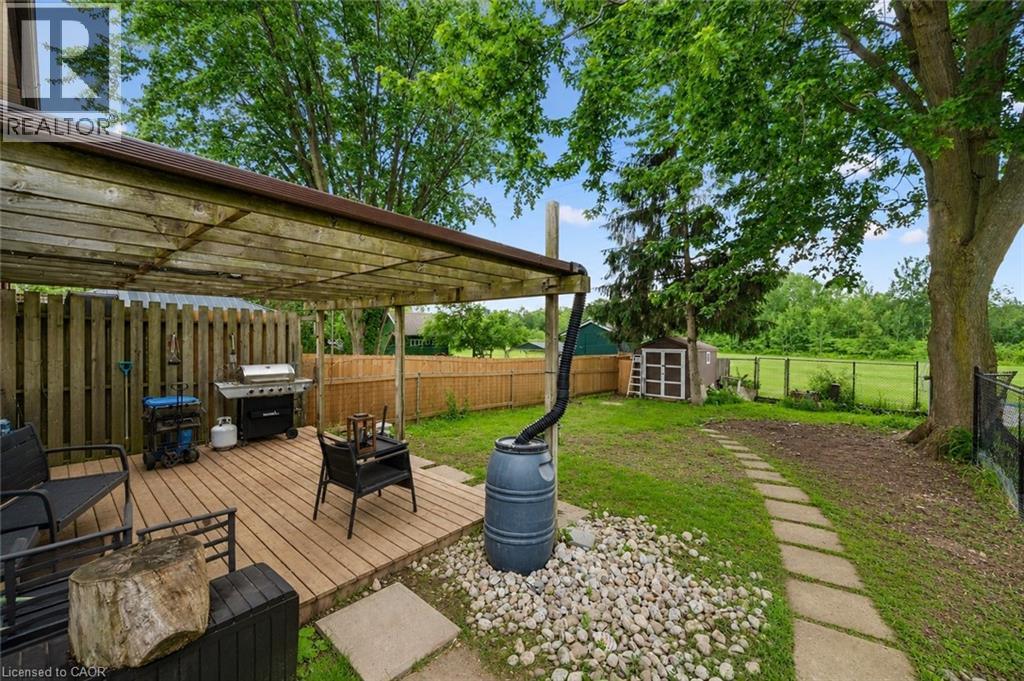 Covered wood-finish deck with a privacy fence, leading to a lawn area with a stepping stone path and a storage shed. digitally enhanced. - 35 Vicmount Drive, Kitchener, ON