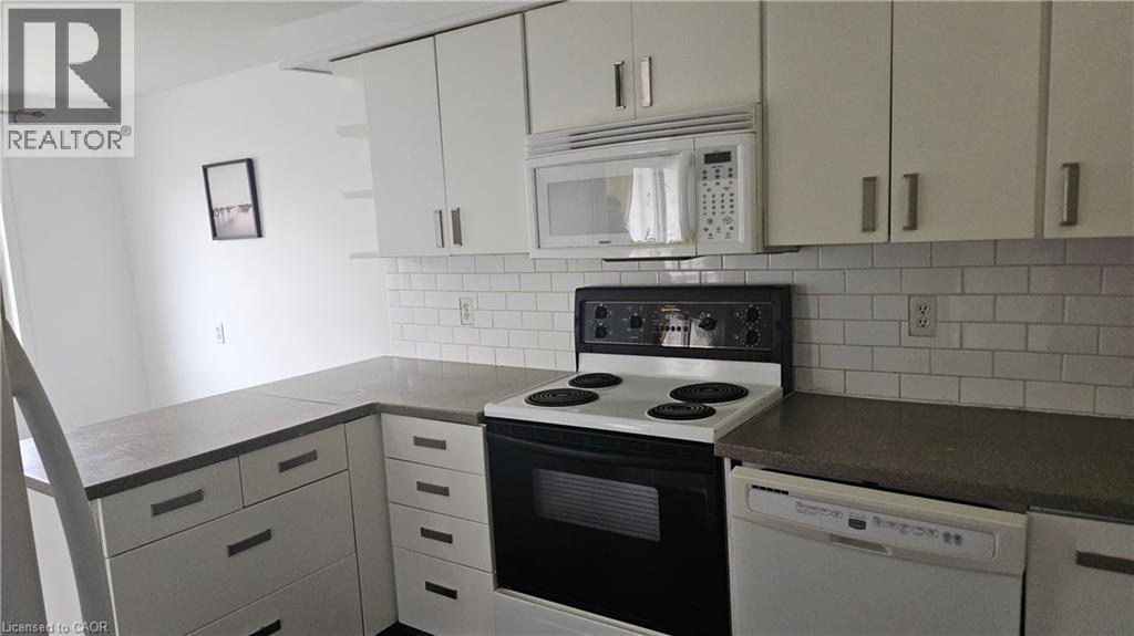 Kitchen featuring white cabinetry with brushed nickel hardware, solid surface countertops, white subway tile backsplash, built-in microwave, and an electric range - 58 Belwood Crescent, Kitchener, ON