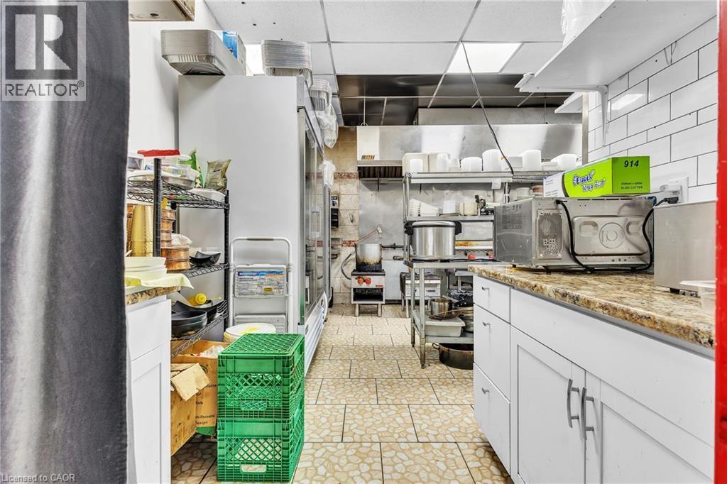 Commercial kitchen featuring tiled flooring, white subway tile backsplash, white cabinetry with silver-tone hardware, and an integrated stainless steel range hood - 155 Highland Road E, Kitchener, ON