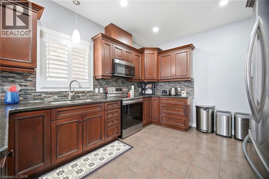 Kitchen featuring dark wood cabinetry, stainless steel appliances, speckled countertops, a mosaic tile backsplash, and ceramic tile flooring - 79 Garinger Crescent, Hamilton, ON