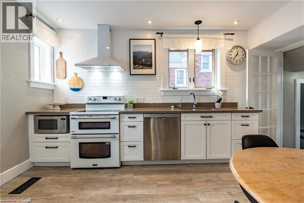 Modern kitchen featuring white shaker cabinetry, stainless steel appliances, wood-finish flooring, and a white tiled backsplash - 134 Bridgeport Road E Unit# Upper, Waterloo, ON