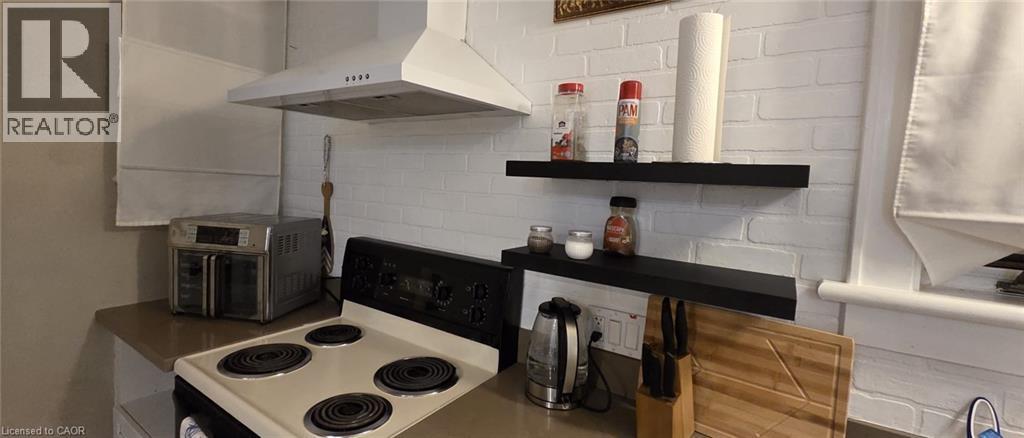 Kitchen area featuring a white brick-style backsplash, a range hood, and a built-in electric stovetop - 134 Bridgeport Road E Unit# Upper, Waterloo, ON