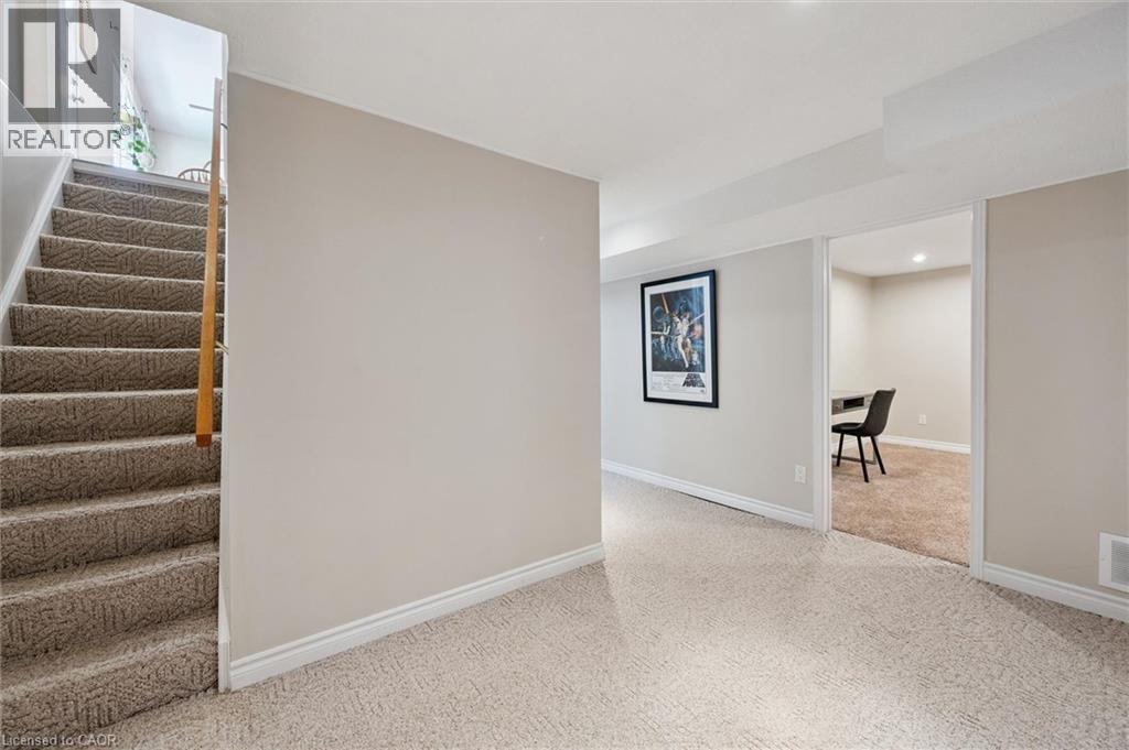 Carpeted staircase with wooden handrail, leading to a carpeted lower level with light-toned walls and white trim - 2 Keewatin Avenue, Kitchener, ON