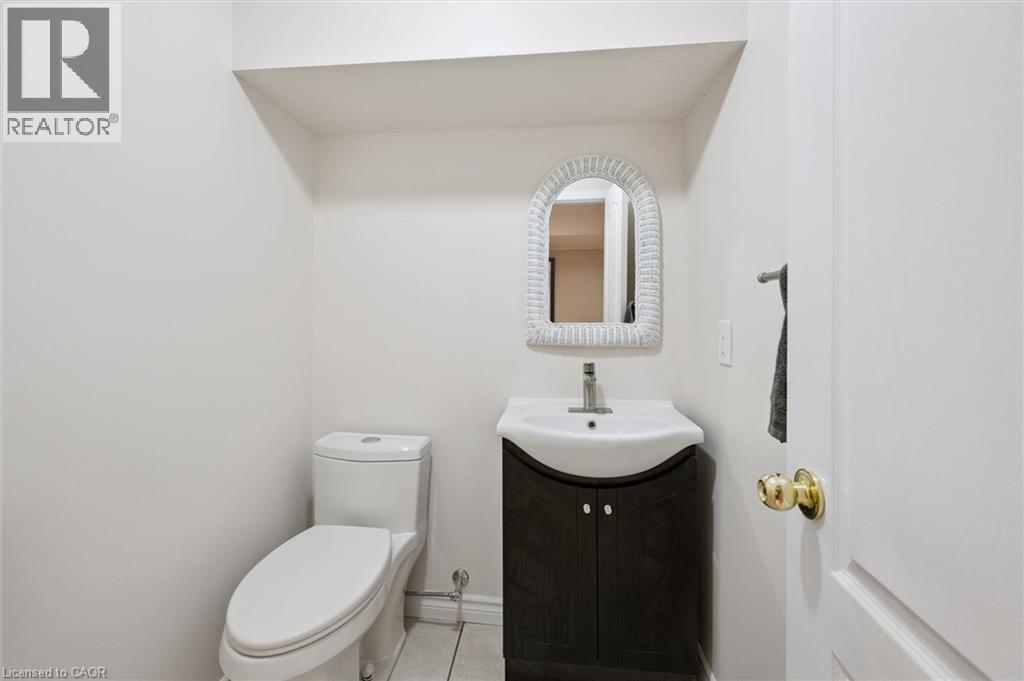 Powder room featuring a sleek white toilet, a vanity with dark wood-finish cabinetry, a white basin, and a contemporary faucet - 2 Keewatin Avenue, Kitchener, ON