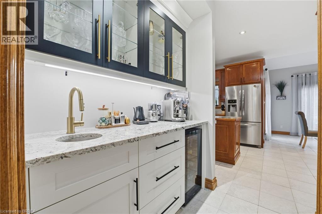 Built-in wet bar featuring white cabinetry, a granite countertop, under-cabinet lighting, a gold-tone faucet, and a beverage cooler - 271 Windham Rd 14, Simcoe, ON