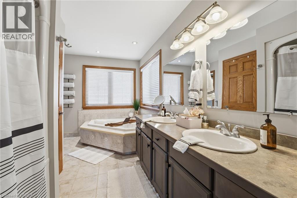 Bathroom featuring a dual vanity with undermount sinks, a built-in tub with a tiled surround, a large mirror, and recessed lighting - 271 Windham Rd 14, Simcoe, ON