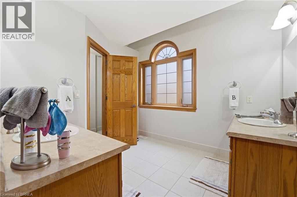 Bathroom featuring a large arched transom window, dual vanity sinks, light wood-finish cabinetry, neutral countertops, and tile flooring - 271 Windham Rd 14, Simcoe, ON