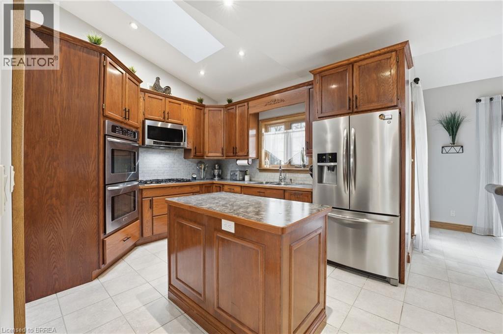 Kitchen featuring wood cabinetry, stainless steel appliances, a central island with a solid surface countertop, white tile flooring, and a skylight - 271 Windham Rd 14, Simcoe, ON