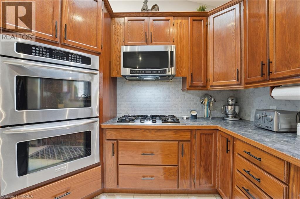 Kitchen featuring stainless steel double wall ovens, a gas cooktop, built-in microwave, wood cabinetry, and a tile backsplash - 271 Windham Rd 14, Simcoe, ON