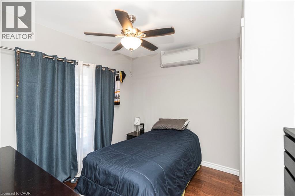 Bedroom featuring wood-finish flooring, a ceiling fan with integrated lighting, and a wall-mounted climate control unit - 38 Fairleigh Avenue N, Hamilton, ON