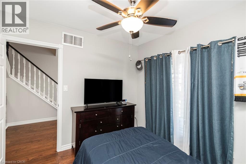 Interior space with wood-finish flooring, a ceiling fan with integrated lighting, and a doorway opening to a staircase with white spindles and a dark handrail - 38 Fairleigh Avenue N, Hamilton, ON