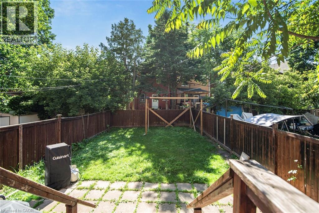 Private backyard with a full perimeter wood fence, featuring a central grass area and a paver stone patio - 38 Fairleigh Avenue N, Hamilton, ON