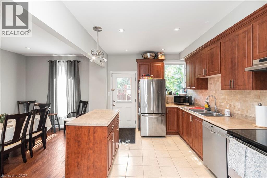 Kitchen featuring wood-finish cabinetry, stainless steel appliances, light-toned tiled flooring, and a stone-look countertop - 38 Fairleigh Avenue N, Hamilton, ON