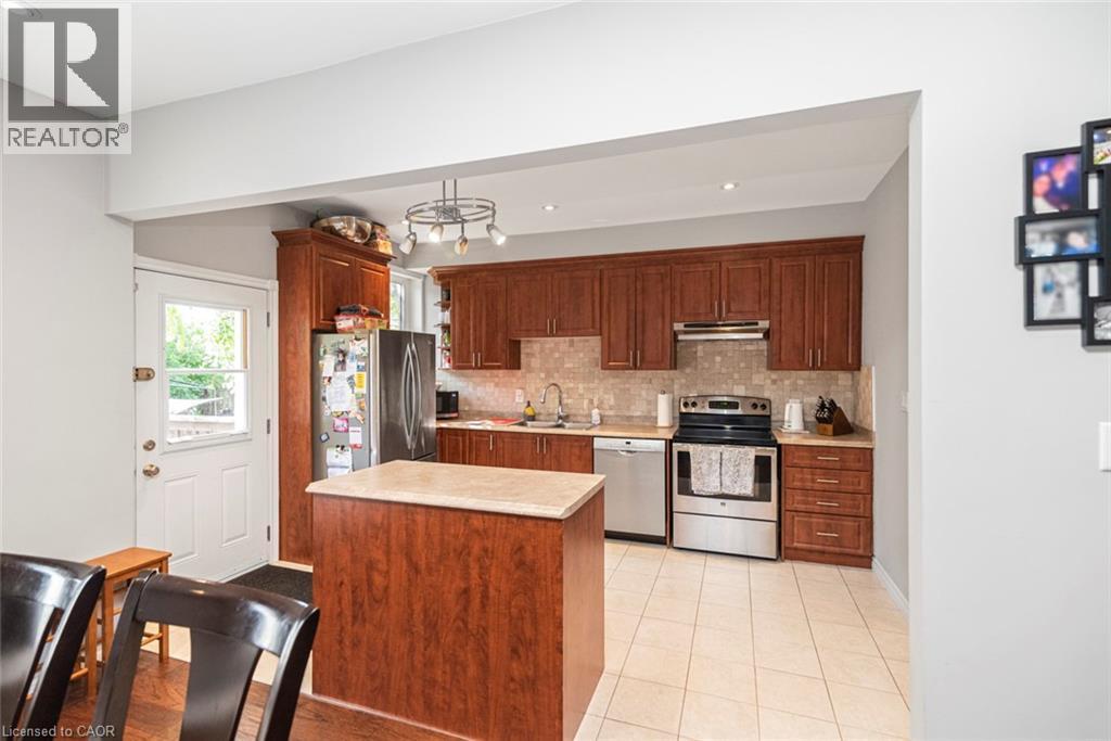 Kitchen featuring wood-finish cabinetry, stainless steel appliances, a center island with a light-toned countertop, and tiled flooring - 38 Fairleigh Avenue N, Hamilton, ON
