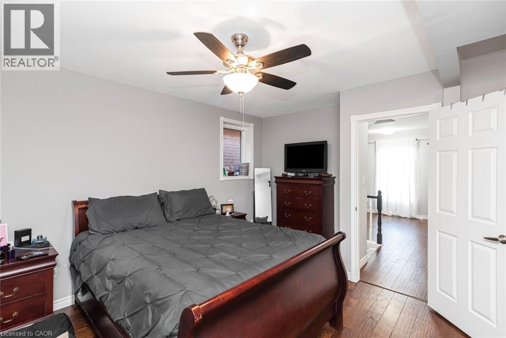 Bedroom featuring wood-finish flooring, a ceiling fan with integrated lighting, and a window with brick exterior visibility - 38 Fairleigh Avenue N, Hamilton, ON