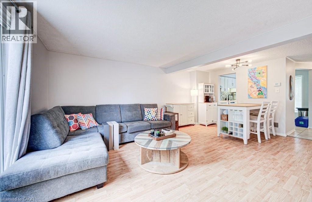Spacious open-concept living area featuring light wood-finish flooring, a dining area with a built-in shelving unit, a large window, and an overhead light fixture - 854 Elgin Street N, Cambridge, ON