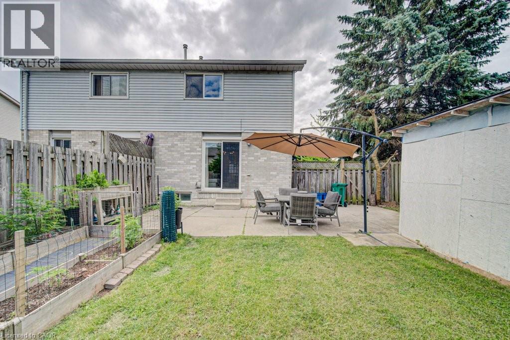 Expansive backyard featuring a concrete patio, sliding glass door access to the interior, a detached storage shed, a wood fence perimeter, and a raised garden bed - 854 Elgin Street N, Cambridge, ON