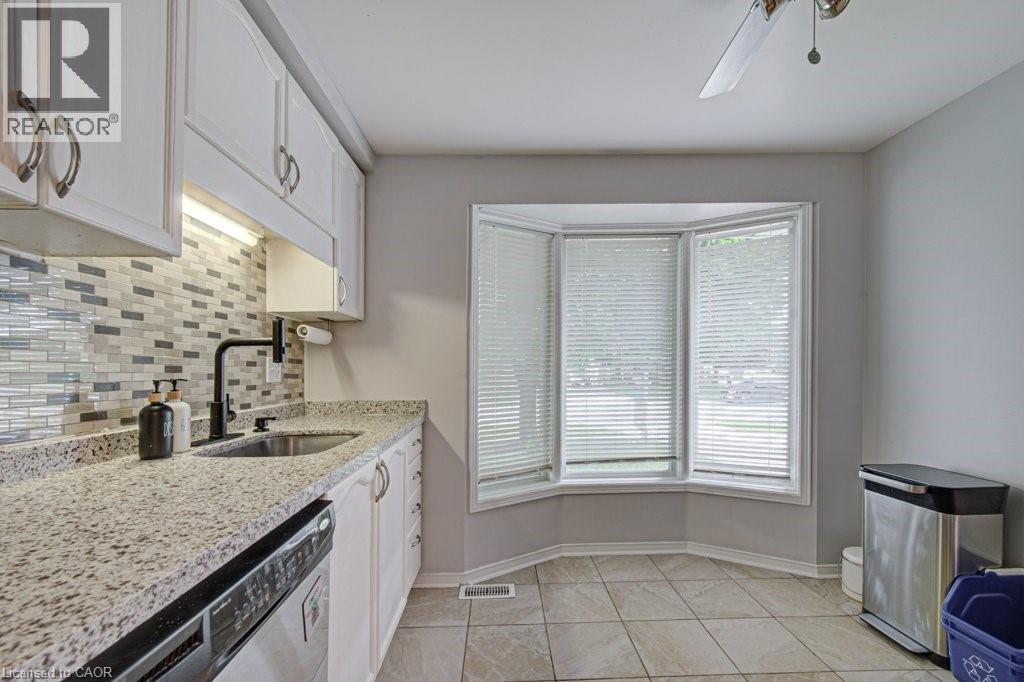 Kitchen featuring a bay window with blinds, white cabinetry, a mosaic tile backsplash, and light-toned countertops - 854 Elgin Street N, Cambridge, ON