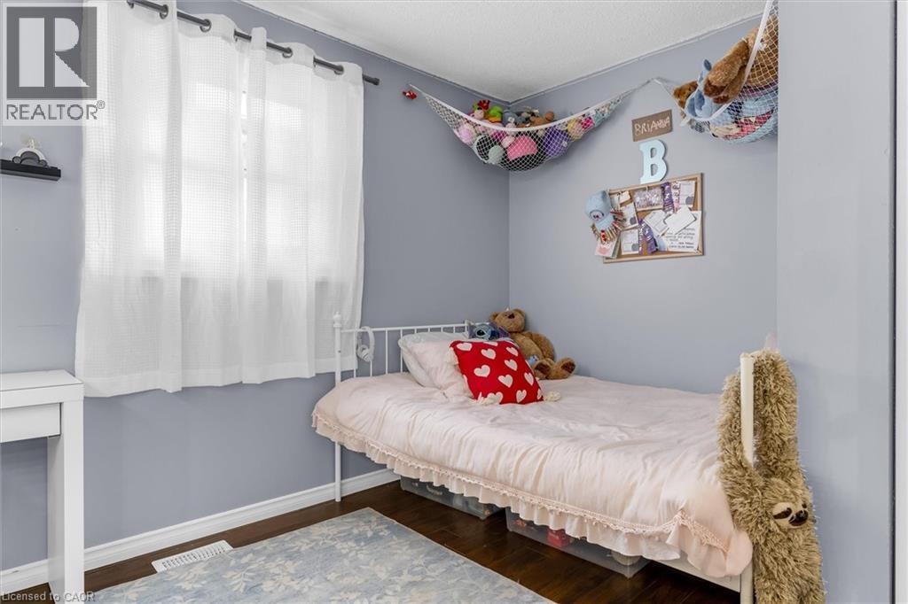 Bedroom featuring light gray walls, dark wood-finish flooring, and a white window with sheer curtains - 338 East 24Th Street, Hamilton, ON