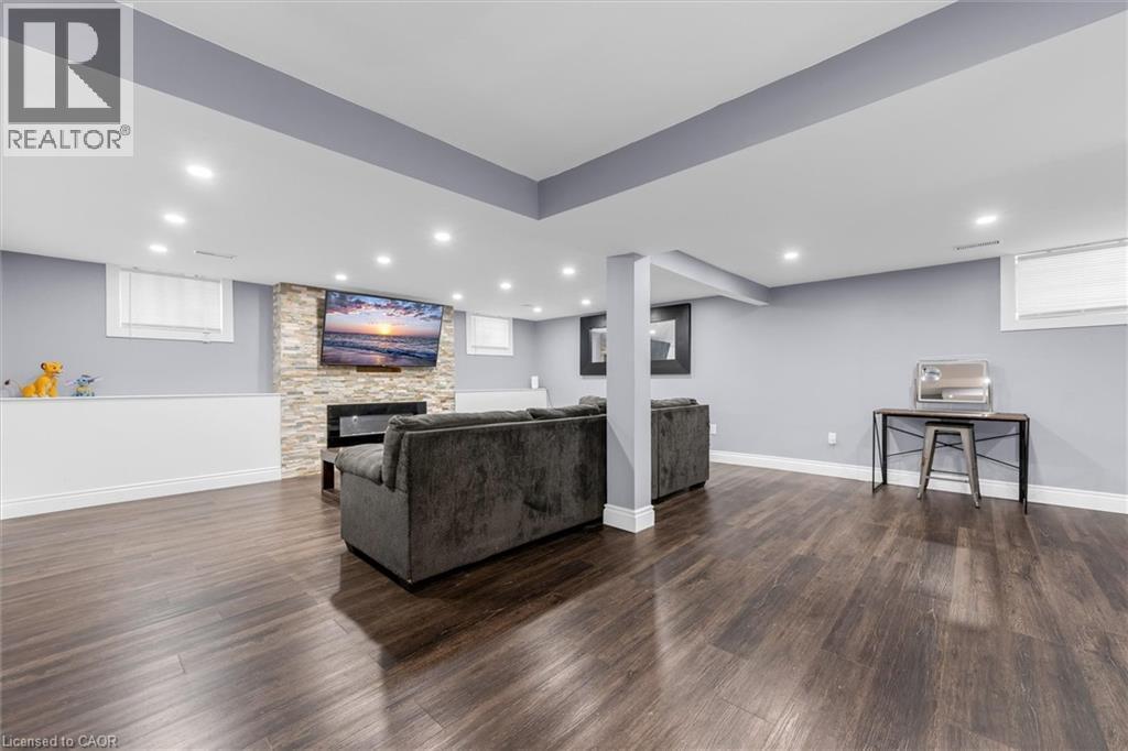 Spacious lower-level entertainment area featuring wood-finish flooring, a stone-clad fireplace, and recessed lighting - 338 East 24Th Street, Hamilton, ON