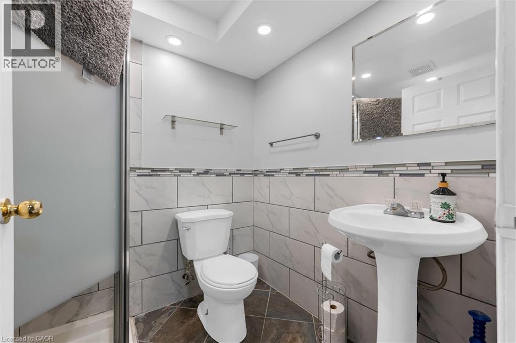 Bathroom featuring a pedestal sink with a single-handle faucet, a toilet, and a tiled accent wall - 338 East 24Th Street, Hamilton, ON