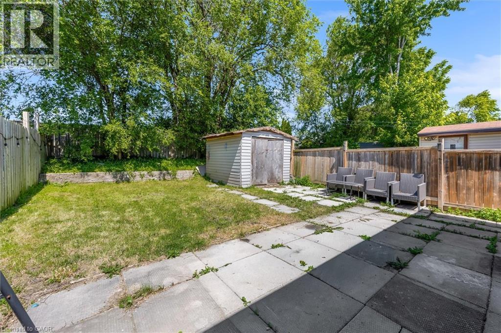 Backyard featuring a concrete paver patio, a separate grassy area, a wooden privacy fence, and a utility shed - 338 East 24Th Street, Hamilton, ON
