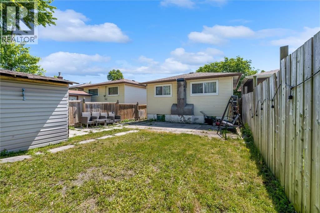 Rear exterior featuring a grass lawn, a wood fence, and a detached shed with horizontal siding - 338 East 24Th Street, Hamilton, ON