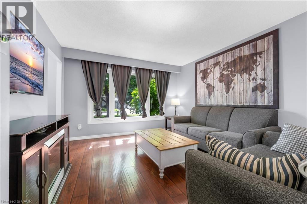 Living area featuring wood-finish flooring, light grey wall tones, and multiple large windows with white trim - 338 East 24Th Street, Hamilton, ON