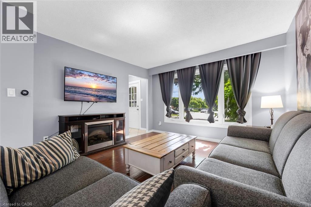Living area featuring wood-finish flooring, a contemporary wall-mounted media console with an integrated electric fireplace, and a large multi-pane window - 338 East 24Th Street, Hamilton, ON