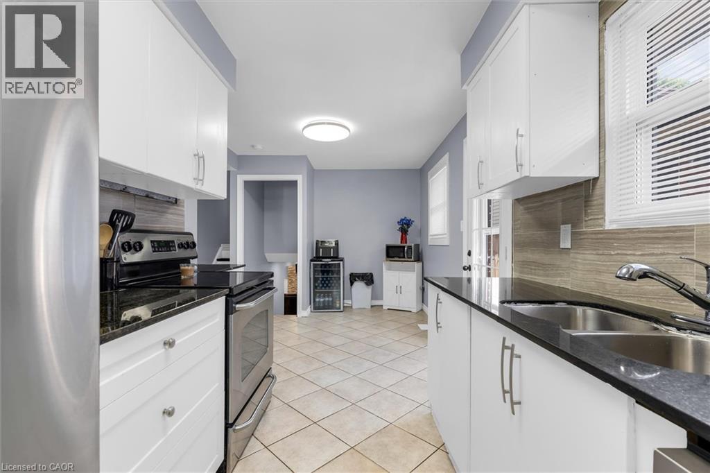 Contemporary kitchen featuring white cabinetry, dark countertops, a stainless steel range, and tile flooring - 338 East 24Th Street, Hamilton, ON