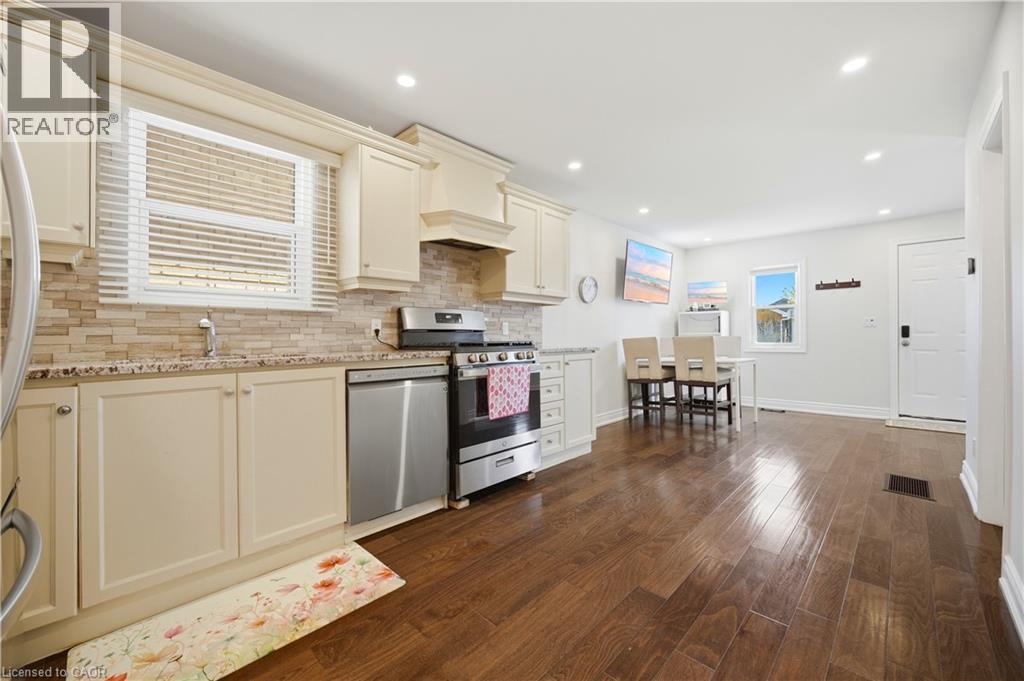 Open concept kitchen featuring cream-colored cabinetry, stone-finish countertops, stainless steel appliances, and wood-finish flooring - 71 Beland Avenue N, Hamilton, ON - Indoor Photo Showing Kitchen With Upgraded Kitchen