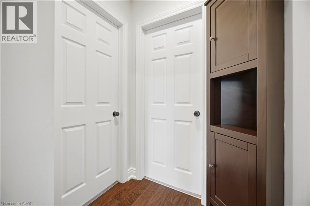 Hallway featuring wood-finish flooring, two white paneled doors with dark hardware, and a built-in dark wood storage cabinet with open shelving - 71 Beland Avenue N, Hamilton, ON - Indoor Photo Showing Other Room
