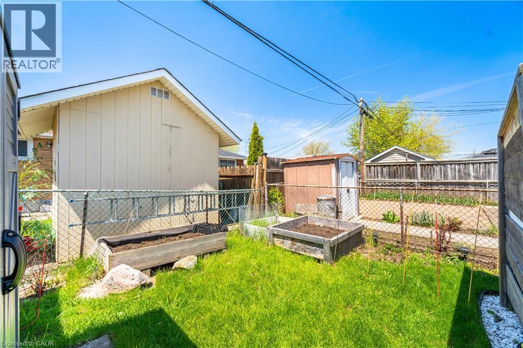 Fenced backyard with established lawn, two raised garden beds, and a storage shed - 71 Beland Avenue N, Hamilton, ON - Outdoor With Exterior