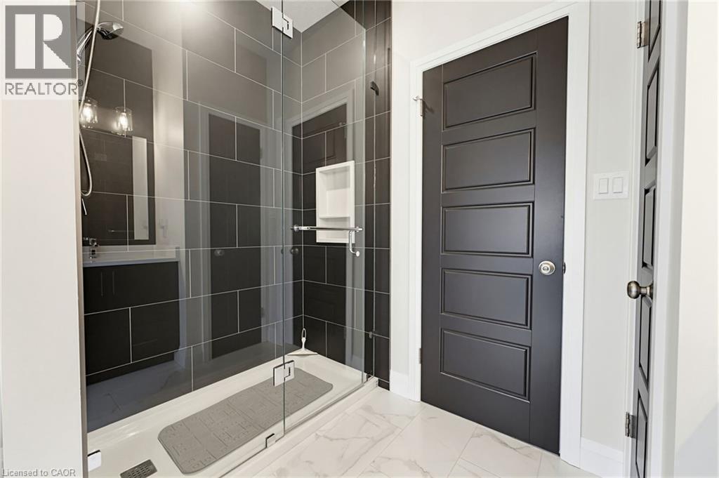 Modern bathroom featuring a glass-enclosed shower with dark tile surround, a built-in shower niche, and a vanity with a rectangular mirror - 37 Gilmer Crescent, Listowel, ON - Indoor Photo Showing Bathroom
