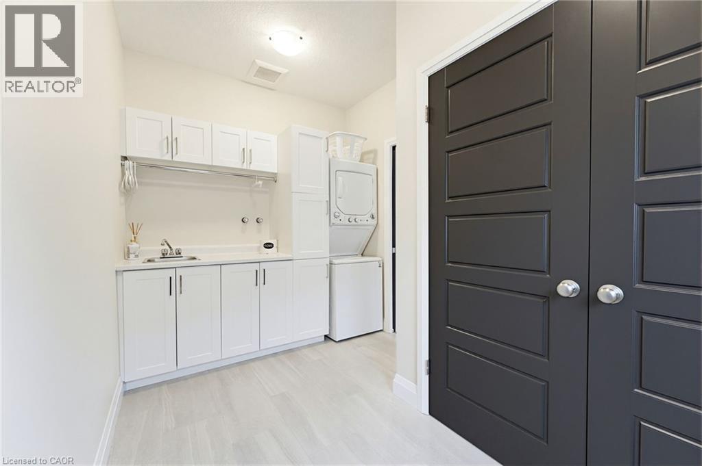 Dedicated laundry area featuring white cabinetry, a built-in sink with countertop, and stacked appliance space - 37 Gilmer Crescent, Listowel, ON - Indoor