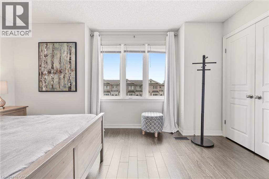 Bright room featuring a large three-panel window, wood-finish flooring, and white baseboards - 4171 Palermo Common, Burlington, ON - Indoor Photo Showing Bedroom