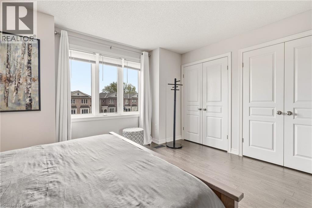 Bright bedroom featuring wood-finish flooring, a multi-pane window with white trim, and two sets of double-door closets with brushed nickel hardware - 4171 Palermo Common, Burlington, ON - Indoor Photo Showing Bedroom