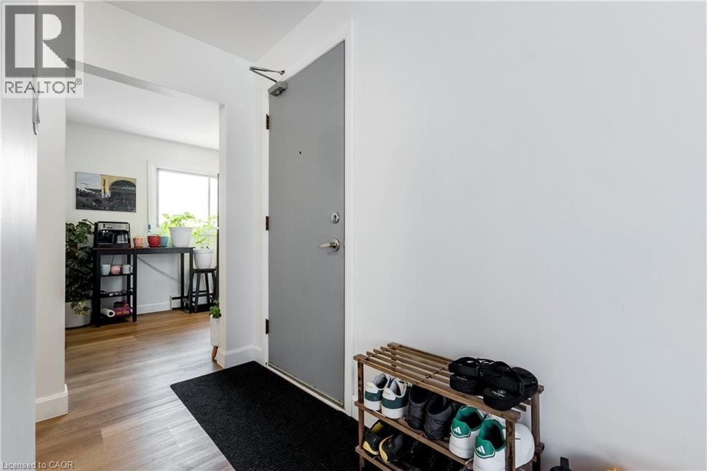 Entryway featuring a solid gray door with a metal door closer, light wood-finish flooring, white baseboards, and a bright white wall - 43 Sixth Avenue, Kitchener, ON - Indoor Photo Showing Other Room