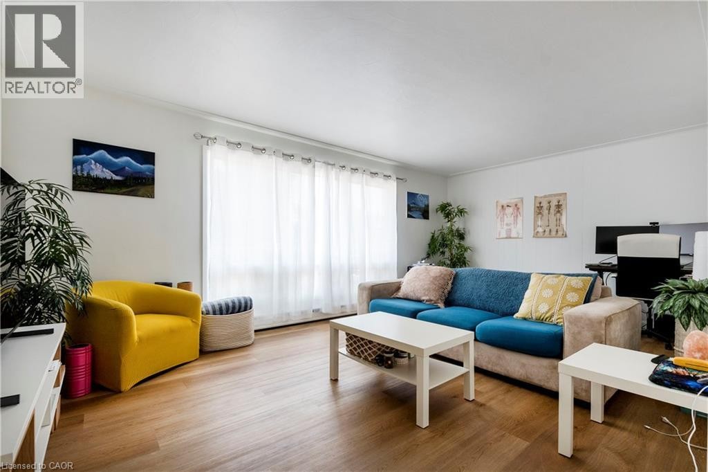 Bright living area featuring wood-finish flooring, white walls, and a large window with white curtains - 43 Sixth Avenue, Kitchener, ON - Indoor Photo Showing Living Room