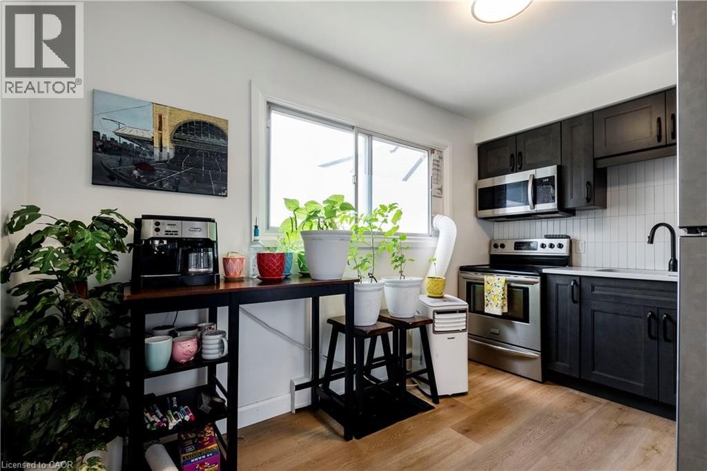 Modern kitchen featuring dark wood-finish cabinetry, stainless steel appliances, white subway tile backsplash, and light wood-finish flooring - 43 Sixth Avenue, Kitchener, ON - Indoor Photo Showing Kitchen