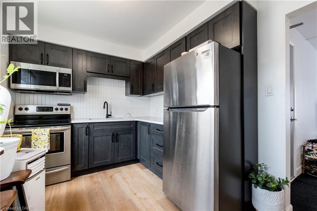 Contemporary kitchen featuring dark wood-finish cabinetry, light-toned countertops, subway tile backsplash, and stainless steel appliances including a refrigerator, range, and microwave - 43 Sixth Avenue, Kitchener, ON - Indoor Photo Showing Kitchen