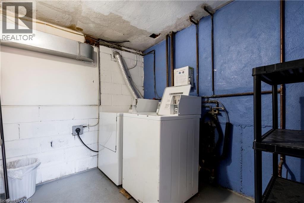 Laundry area featuring white block walls, concrete flooring, exposed utility piping, and a washer and dryer set - 43 Sixth Avenue, Kitchener, ON - Indoor Photo Showing Laundry Room